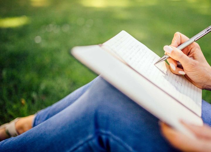 Uma mulher sentado na grama escrevendo um diário.
