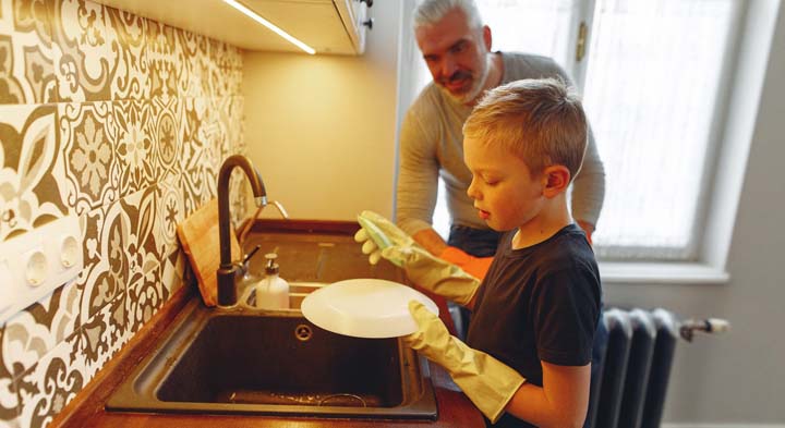Uma criança lavando louças para ajudar nas tarefas da casa