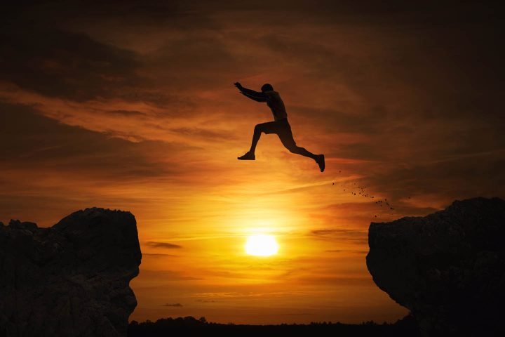 Um homem corajoso pulando sobre uma fenda entre duas rochas