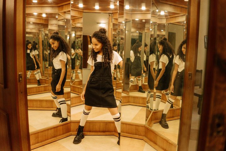Uma garota adolescente em uma sala de espelhos olhando para suas múltiplas imagens