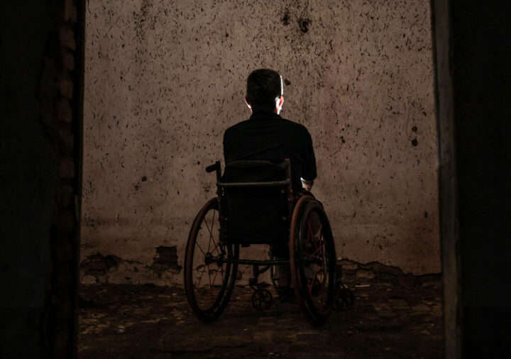 Um homem idoso sentado em uma cadeira de rodas em um ambiente sombrio