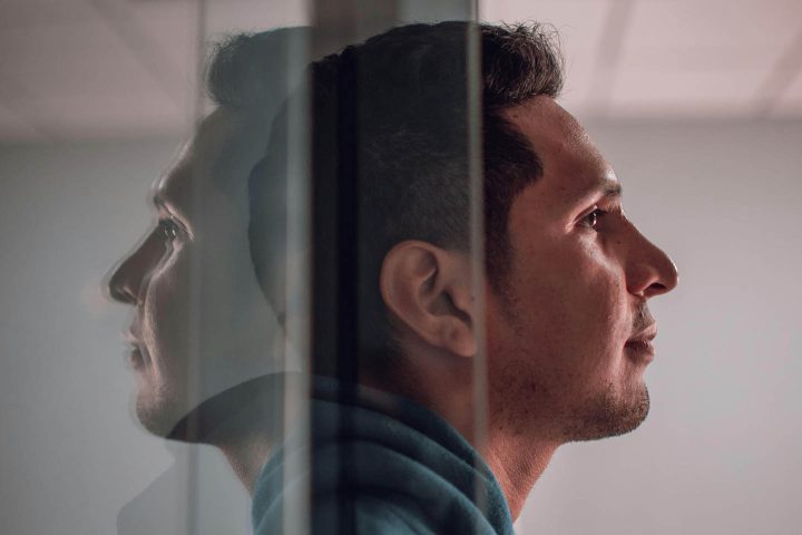 Um homem saindo de uma porta de vidro, deixando o reflexo de seu rosto para trás.