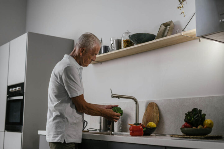 Um homem idoso lavando brócolis e outros vegetais