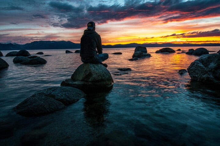Um jovem observando o pôr do sol na praia e refletindo sobre sua vida
