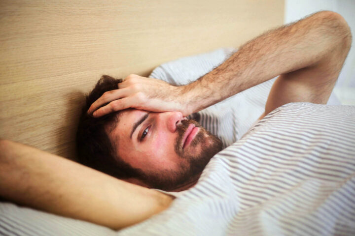 Um homem está deitado na cama com dor de cabeça