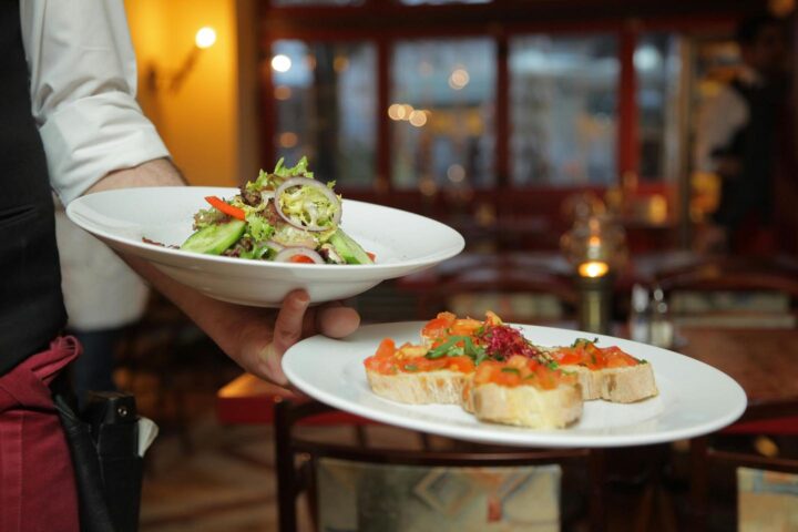 Um garçom no restaurante trazendo um prato de salada e pães com vegetais