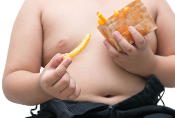 Um garoto obeso comendo batatas fritas